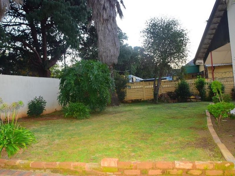 A private rear garden featuring a lawn area, established trees, and perimeter boundary walls with brick edging.