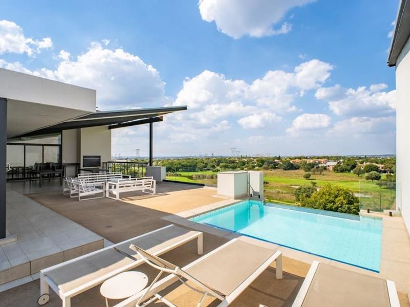A modern elevated patio area featuring a private swimming pool with glass balustrades and expansive views over the surrounding landscape.