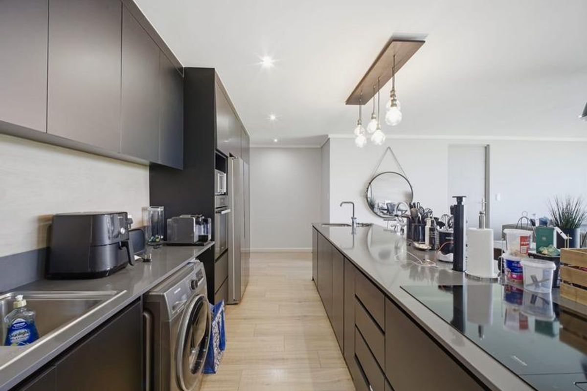 Modern kitchen featuring sleek dark cabinetry, stone countertops, integrated appliances, and a central island with an induction hob and pendant lighting.