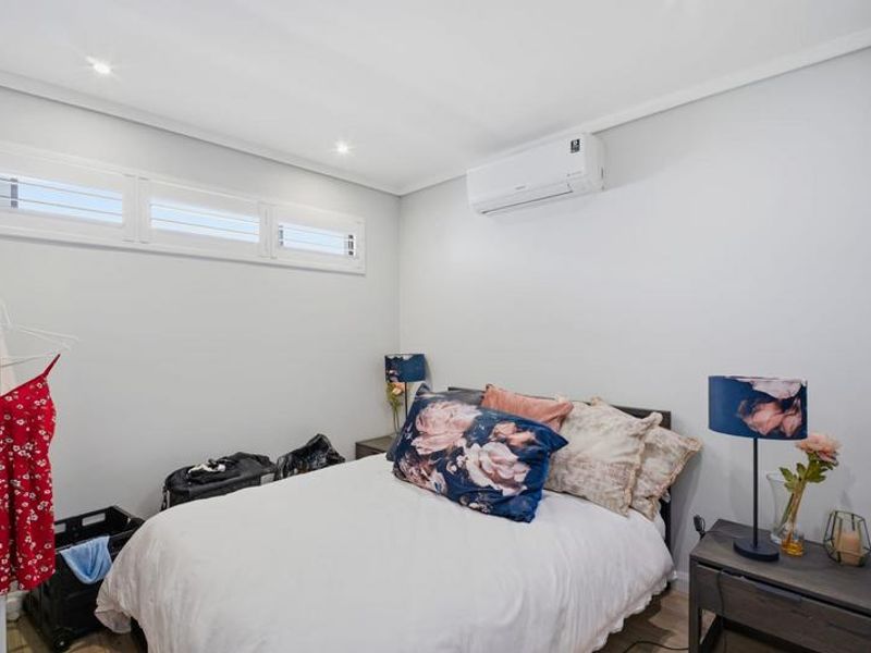 A well-maintained bedroom featuring recessed downlights, a wall-mounted split-system air conditioner, and plantation shutters.