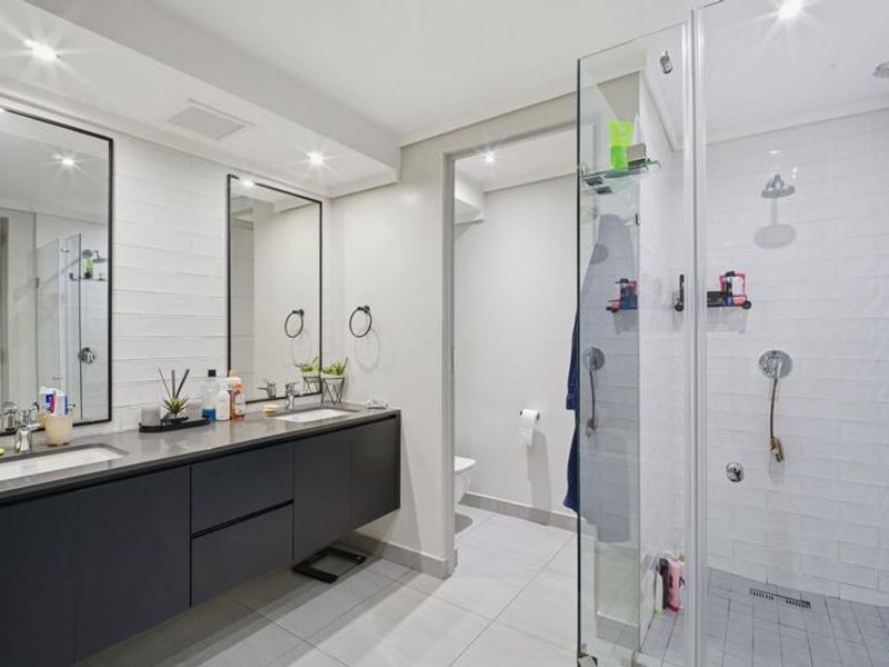 Modern bathroom featuring a sleek double vanity with dark cabinetry, subway tile wall finishes, and a spacious walk-in shower with a glass enclosure.