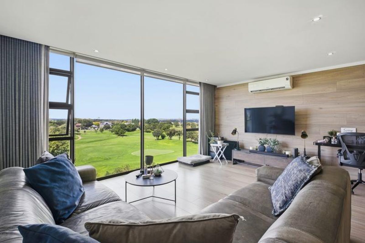 A bright, modern living room featuring floor-to-ceiling windows with expansive golf course views, timber-look wall paneling, and integrated air conditioning.