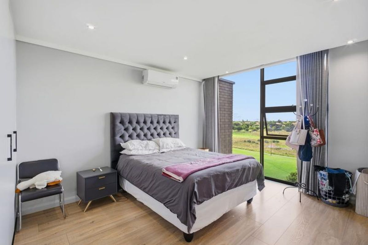 A bright and modern bedroom featuring laminate flooring, recessed lighting, a wall-mounted air conditioning unit, and large windows with scenic views.