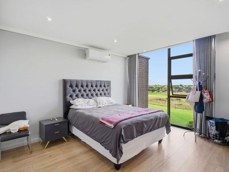 A bright and modern bedroom featuring laminate flooring, recessed lighting, a wall-mounted air conditioning unit, and large windows with scenic views.
