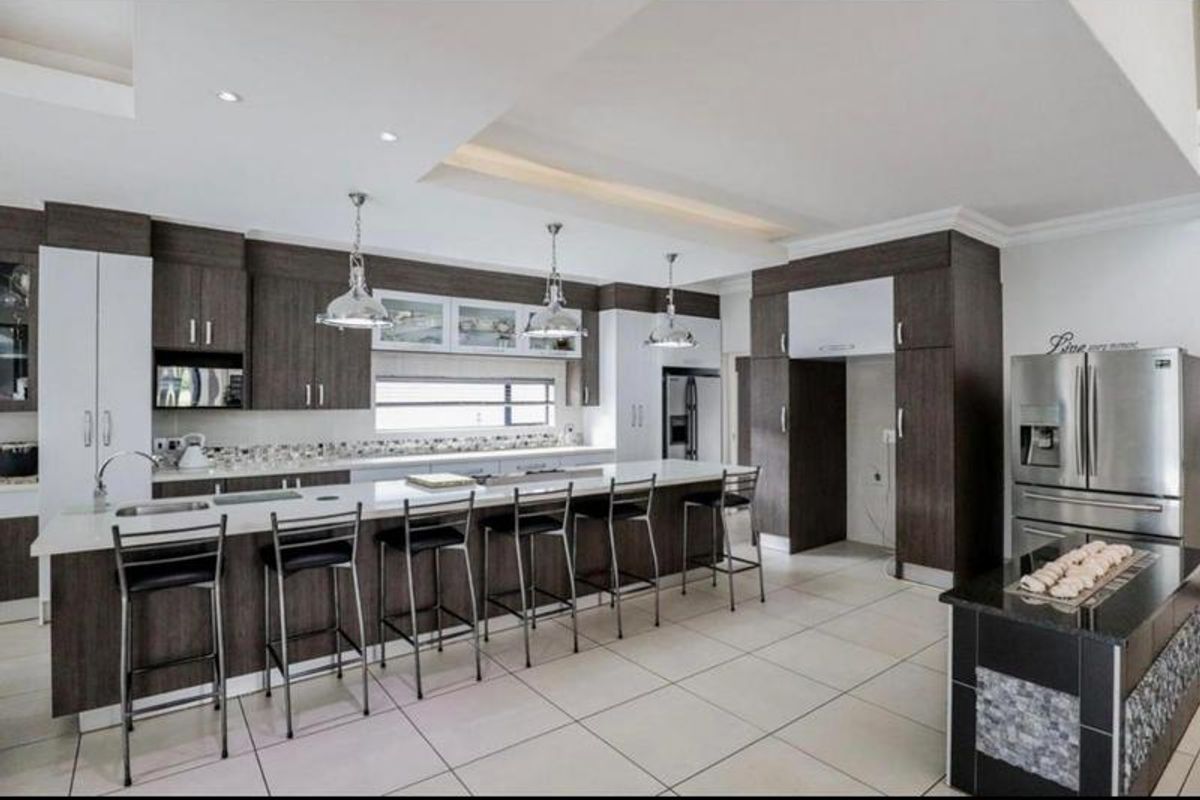 Modern kitchen featuring a large island with breakfast bar seating, dark wood cabinetry, quartz countertops, and integrated stainless steel appliances.