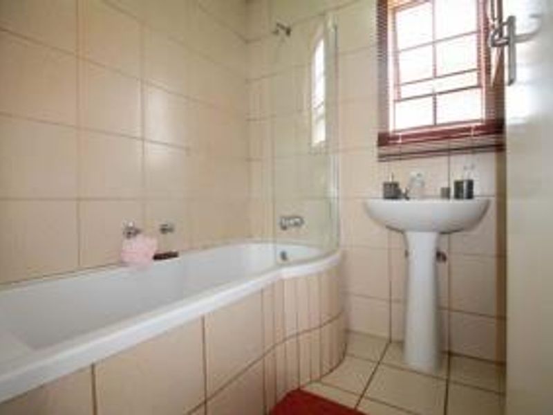 A functional bathroom featuring a pedestal basin, a bathtub with an integrated glass shower screen, and neutral wall and floor tiling.