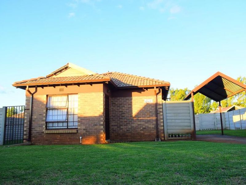A single-story brick house featuring a tiled roof, aluminium window frames, and an attached carport, set within a fenced yard.
