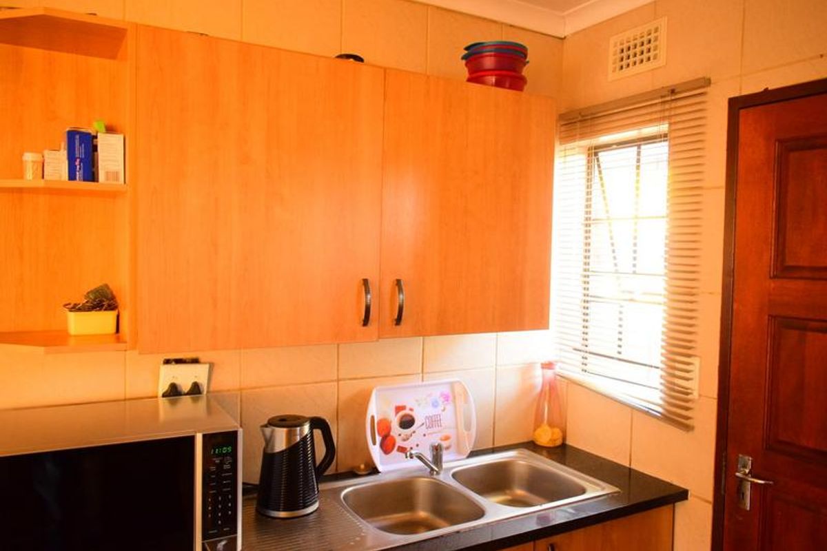 A functional kitchen area featuring light wood-tone cabinetry, a double stainless steel sink with mixer tap, and tiled splashbacks.