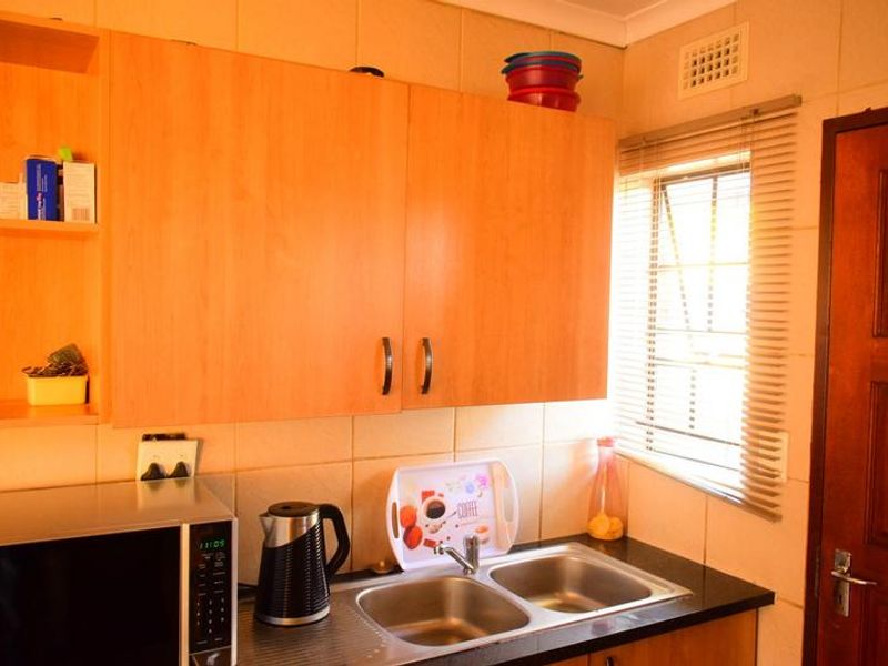 A functional kitchen area featuring light wood-tone cabinetry, a double stainless steel sink with mixer tap, and tiled splashbacks.