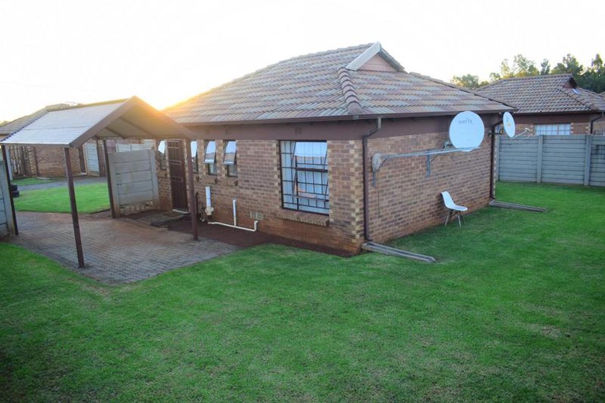 Rear view of a brick house featuring a tiled roof, attached carport, paved driveway, and a private garden area with perimeter walling.