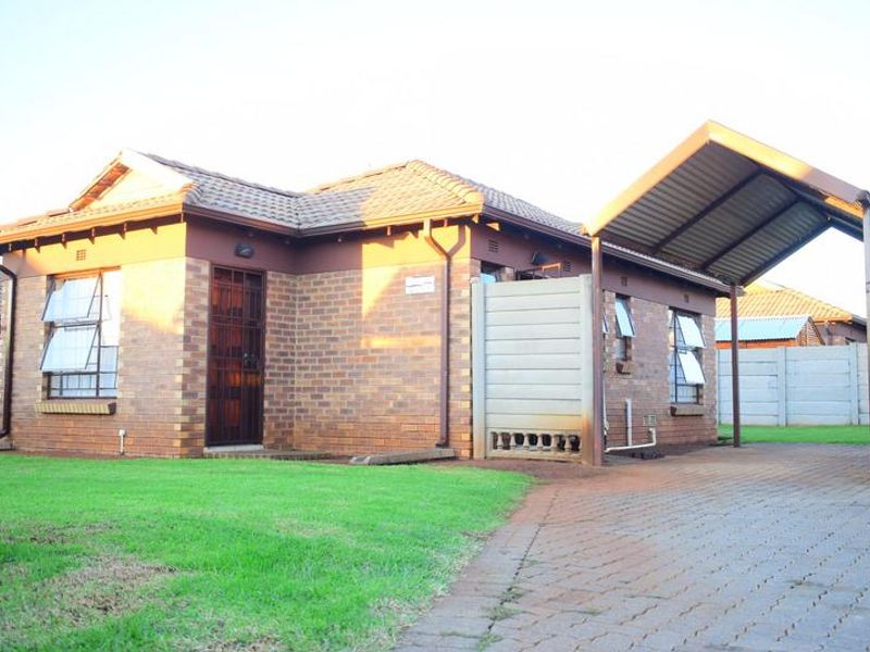 A well-maintained face brick house featuring a tiled roof, paved driveway, and a convenient attached carport, set within a neat residential garden.