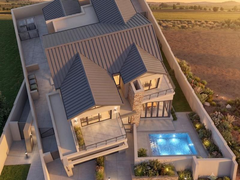 Aerial view of a modern residential property featuring a metal roof, swimming pool, stone accents, and landscaped outdoor areas at sunset.