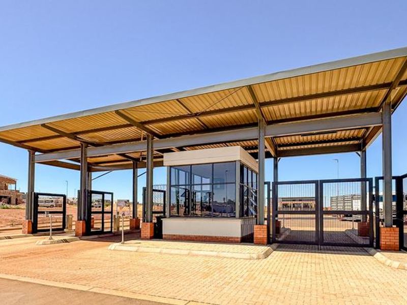 A modern security entrance gatehouse featuring a metal roof structure, steel support columns, and automated security gates at the estate entrance.