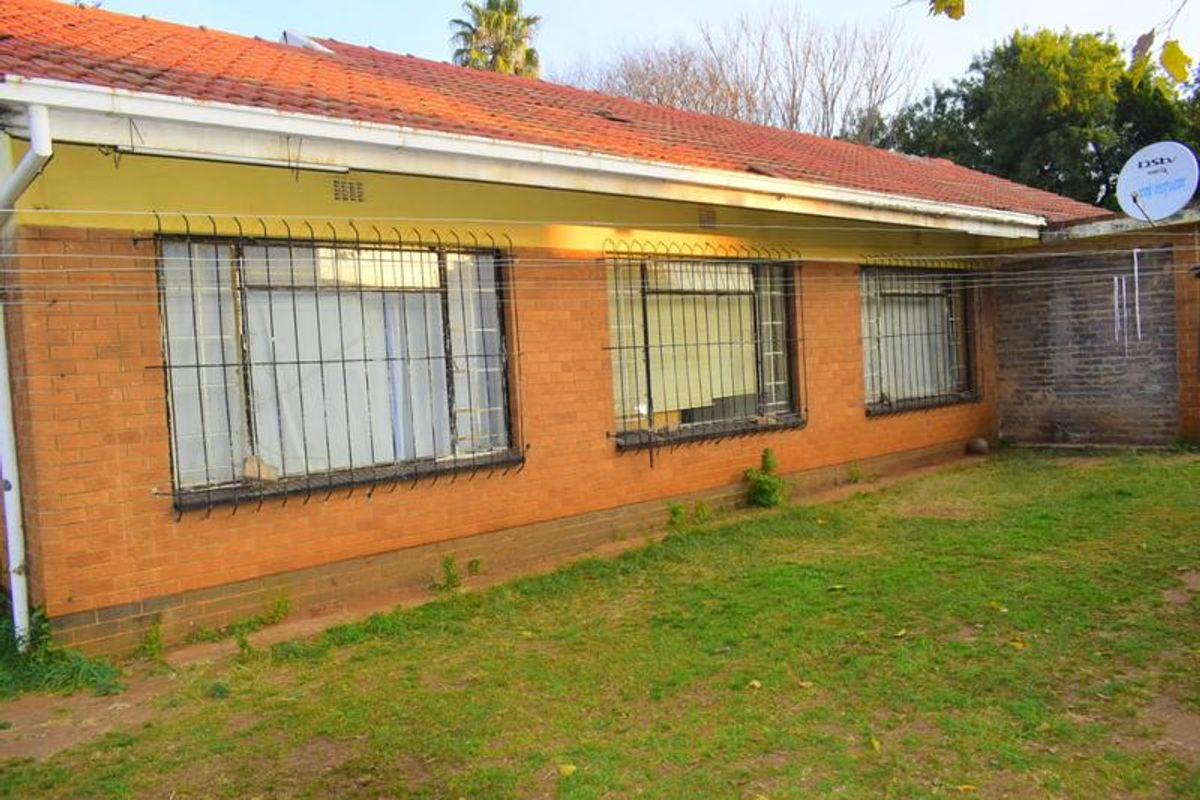 Rear view of a single-story brick house featuring a tiled roof, security bars on windows, and a surrounding lawn area.