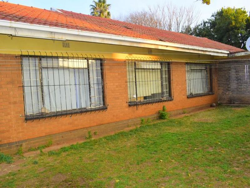 Rear view of a single-story brick house featuring a tiled roof, security bars on windows, and a surrounding lawn area.