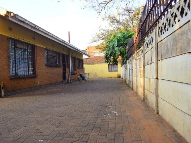Rear exterior view of the property featuring a paved driveway, brick facade, and a precast concrete boundary wall with security fencing.