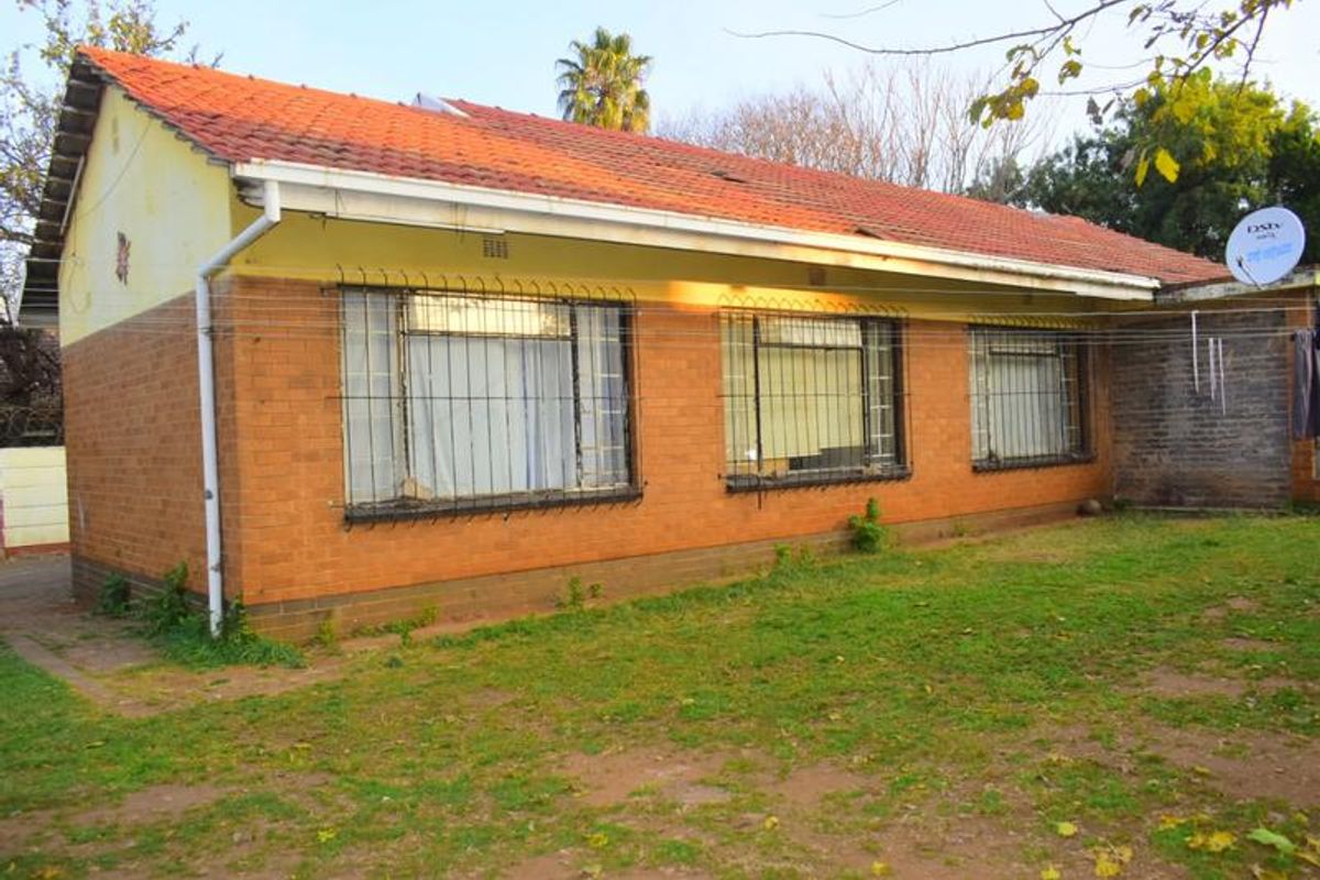 Rear view of a single-story facebrick house featuring a terracotta tiled roof, security bars on windows, and an expansive garden area.