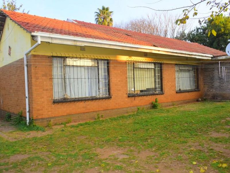 Rear view of a single-story facebrick house featuring a terracotta tiled roof, security bars on windows, and an expansive garden area.