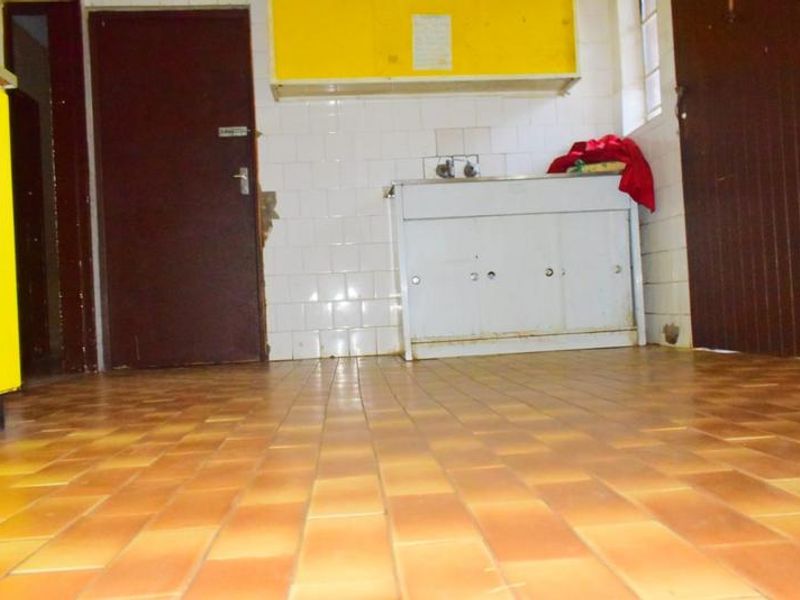 A dated kitchen area featuring tiled flooring, wall-mounted cabinetry, and a basic sink unit, offering significant potential for renovation and modernization.