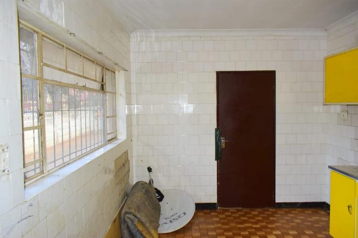 A dated kitchen area featuring tiled walls, metal window frames, and original cabinetry, requiring renovation to modernize the space.