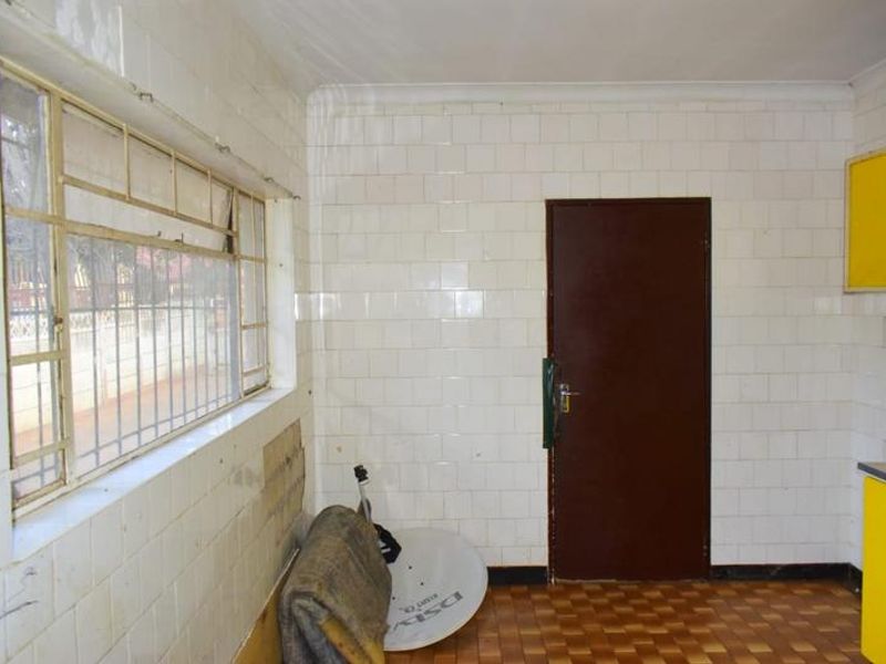 A dated kitchen area featuring tiled walls, metal window frames, and original cabinetry, requiring renovation to modernize the space.
