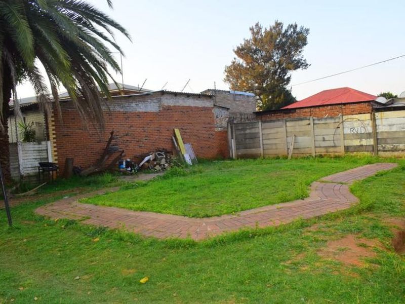A rear garden area featuring a paved walkway, brick and precast concrete boundary walls, and electric fencing.