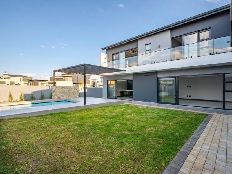 Modern rear exterior featuring a swimming pool, landscaped lawn, paved walkway, and a covered patio area with large sliding doors leading to the interior.