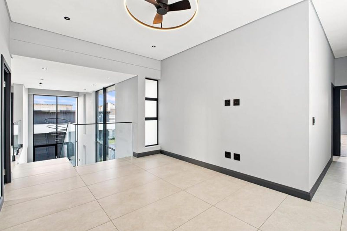 A bright and modern open-plan living area featuring large windows, sleek tiled flooring, a contemporary ceiling fan, and a glass balustrade overlooking the lower level.