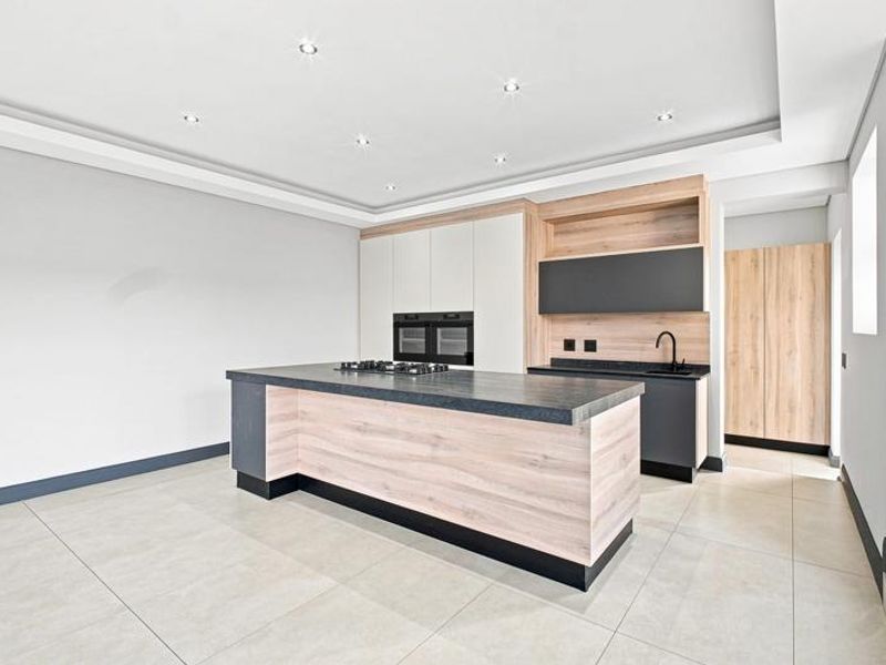Modern kitchen featuring a central island, built-in oven, gas cooktop, sleek cabinetry, and high-quality tiled flooring in a bright, open-plan space.