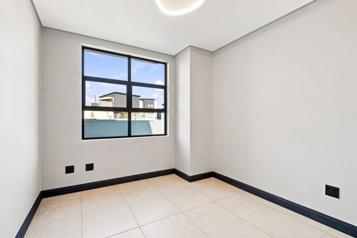 A bright, modern, and empty bedroom featuring neutral tiled flooring, clean white walls, and a large black-framed window providing natural light.