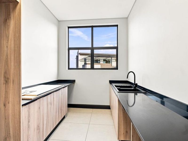 A modern, clean scullery featuring sleek wood-finish cabinetry, dark stone countertops, and a contemporary black sink fixture with ample natural light.