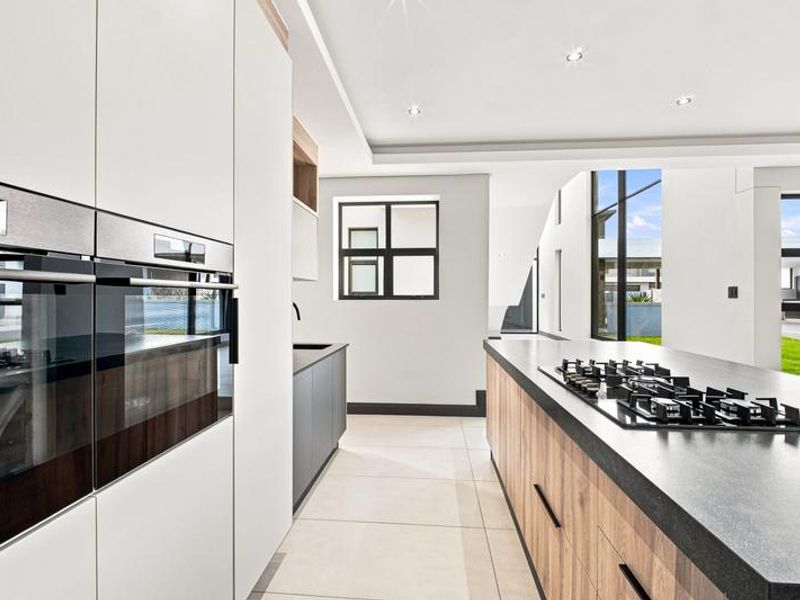 Modern kitchen featuring a large island with a gas cooktop, built-in double ovens, sleek cabinetry, and high-quality stone countertops in an open-plan layout.
