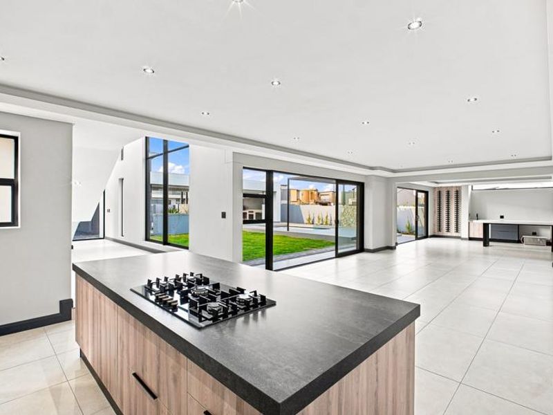 Spacious open-plan living area featuring a modern kitchen island with gas cooktop, tiled floors, and large sliding doors opening to the garden.