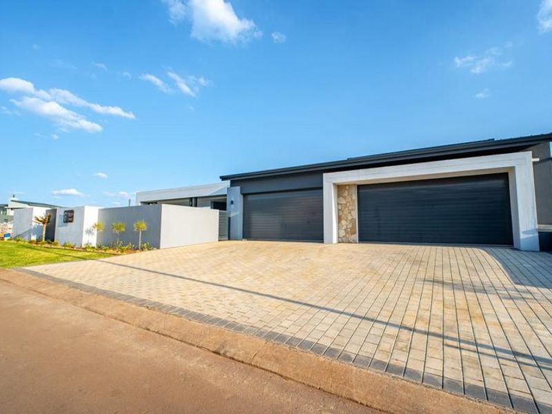 Modern front elevation featuring a double garage with dark roller doors, stone cladding accents, and a spacious paved driveway.