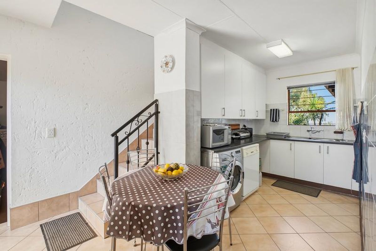 A functional kitchen featuring white cabinetry, tiled flooring, and an integrated staircase with a metal railing, providing a practical layout for daily use.