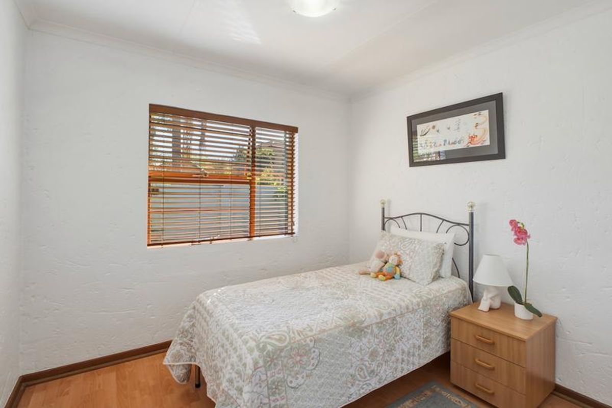A bright bedroom featuring laminate flooring, textured walls, and venetian blinds, providing a clean and functional living space.