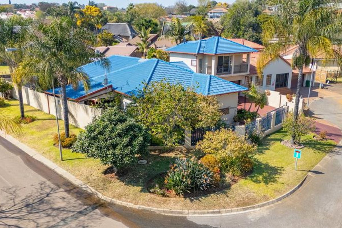 An elevated aerial view of a residential property featuring a blue tiled roof, established garden, and perimeter walling on a corner plot.