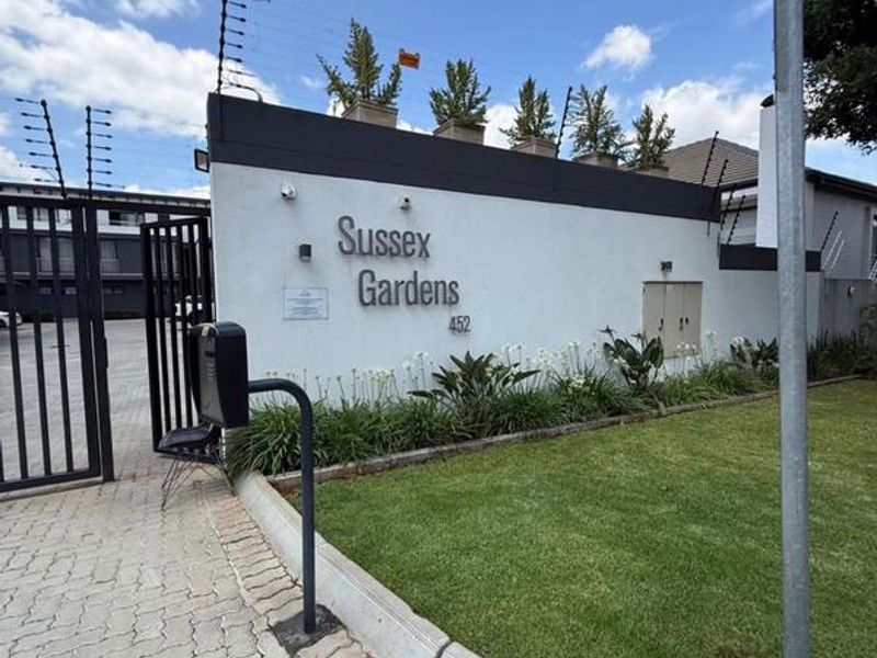 Front entrance view of Sussex Gardens apartment complex featuring secure gated access, electric fencing, and well-maintained garden landscaping.