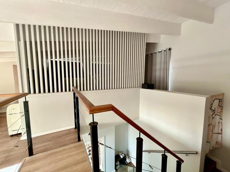 A bright landing area featuring a modern slatted timber room divider, exposed ceiling beams, and a staircase with a timber handrail and metal balustrade.