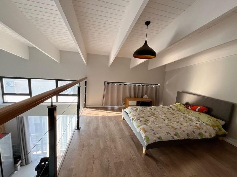 A spacious mezzanine bedroom featuring exposed white timber beams, wood-look laminate flooring, and a modern metal balustrade overlooking the lower level.