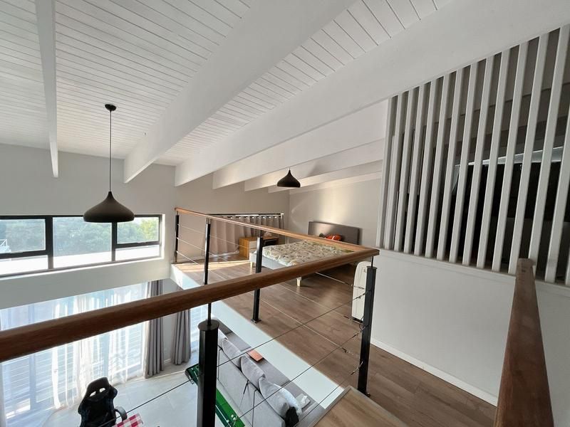 A mezzanine bedroom area featuring vaulted timber ceilings, laminate flooring, and a modern timber slatted screen overlooking the lower living space.