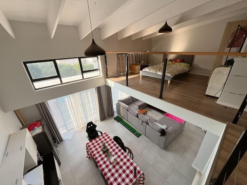 Spacious open-plan apartment featuring a mezzanine bedroom level, high exposed beam ceilings, and a bright living area with large windows.