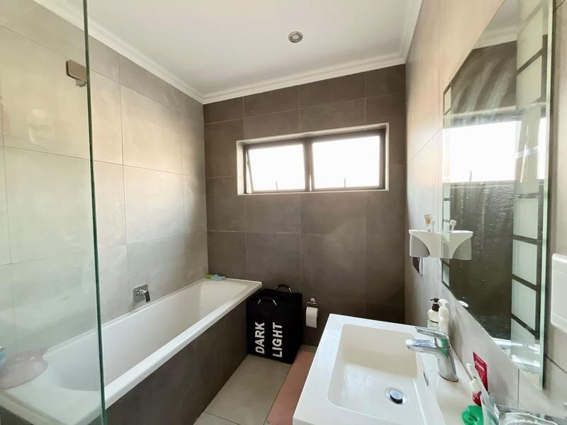 Modern bathroom featuring a built-in bathtub with a glass screen, wall-mounted basin, and neutral floor-to-ceiling tiling.