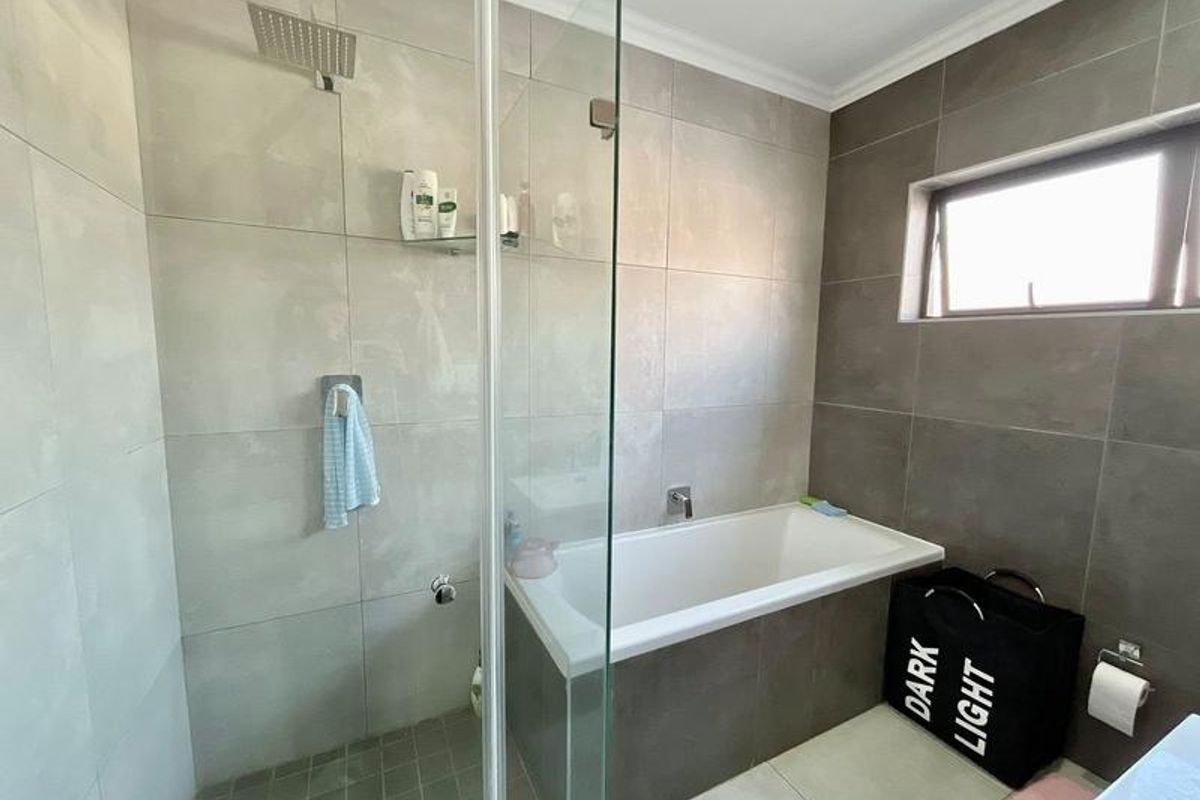 Modern bathroom featuring a combined shower and bathtub area with glass screen, neutral wall tiling, and a functional top-hung window for ventilation.