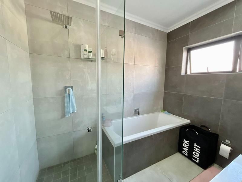 Modern bathroom featuring a combined shower and bathtub area with glass screen, neutral wall tiling, and a functional top-hung window for ventilation.