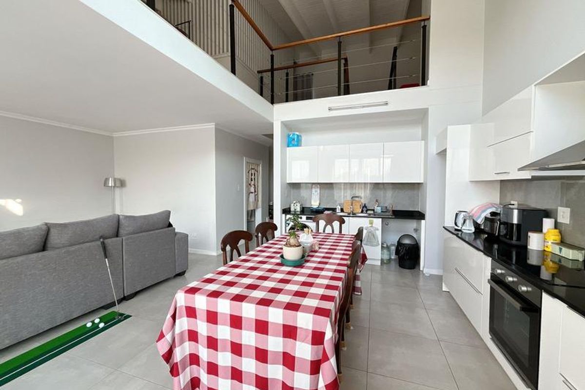 Spacious open-plan living and kitchen area featuring high ceilings, a mezzanine level, modern white cabinetry, and sleek black granite countertops.