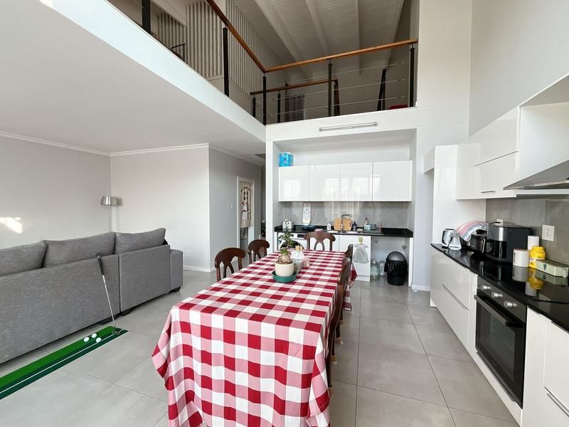 Spacious open-plan living and kitchen area featuring high ceilings, a mezzanine level, modern white cabinetry, and sleek black granite countertops.