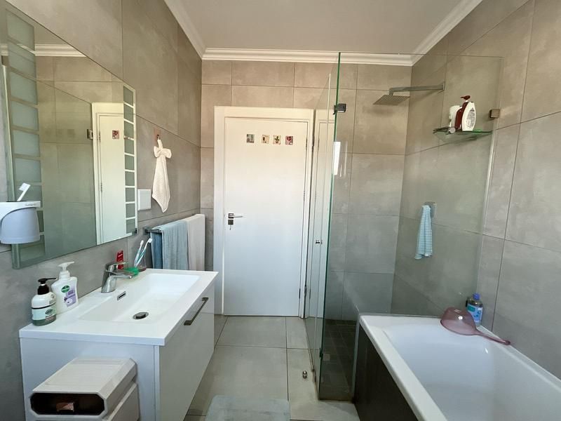Modern bathroom featuring a vanity with basin, a glass-enclosed shower, and a bathtub, finished with neutral wall and floor tiling.