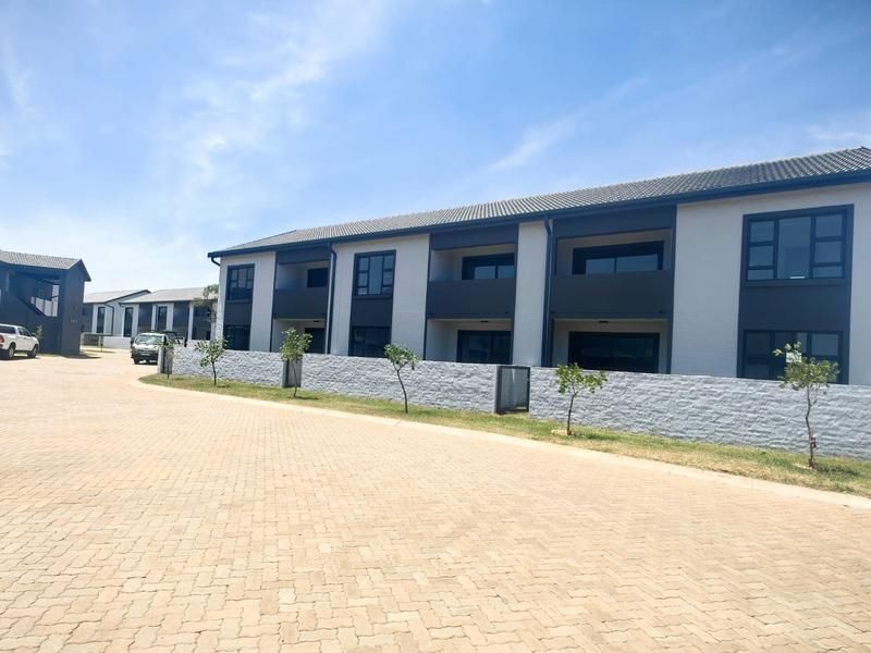 A modern apartment complex exterior featuring paved driveway access, stone boundary walls, and multi-level units with private balconies.