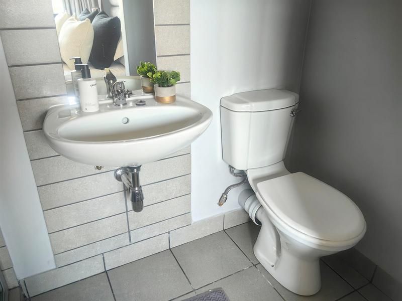 A compact bathroom featuring a wall-mounted basin with chrome fixtures and a standard toilet, finished with tiled splashbacks and flooring.